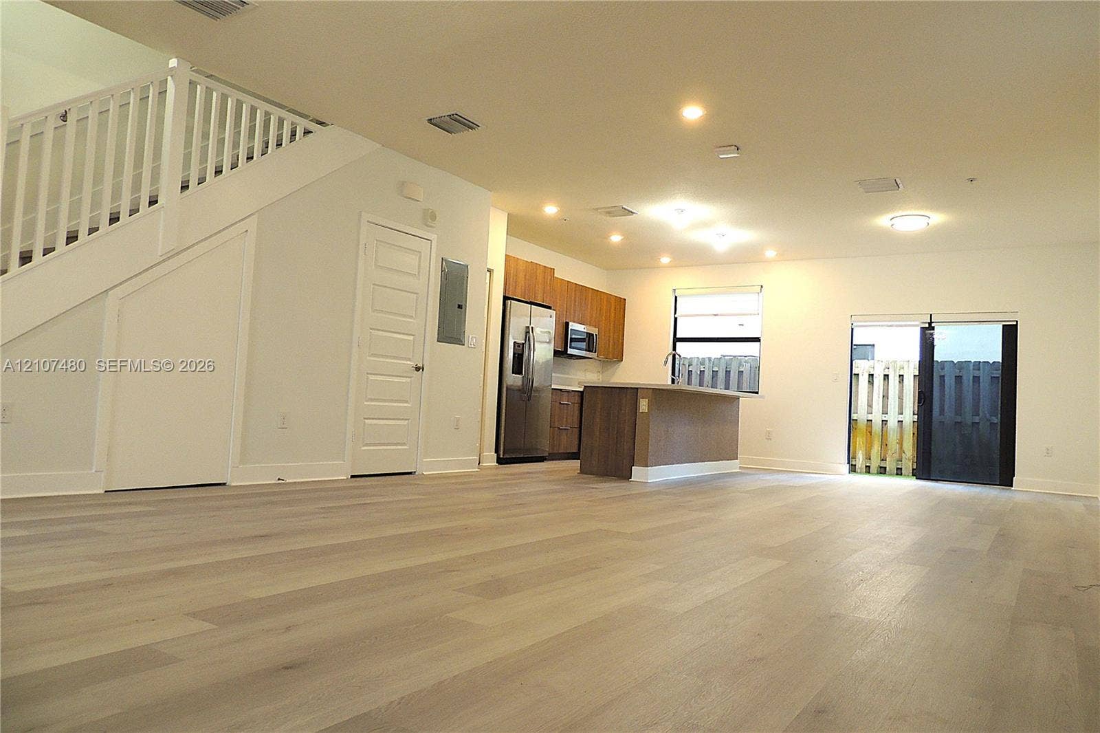 Open floor plan featuring wood-finish flooring, recessed lighting, a central kitchen island, wood-finish cabinetry, and a staircase with a white railing