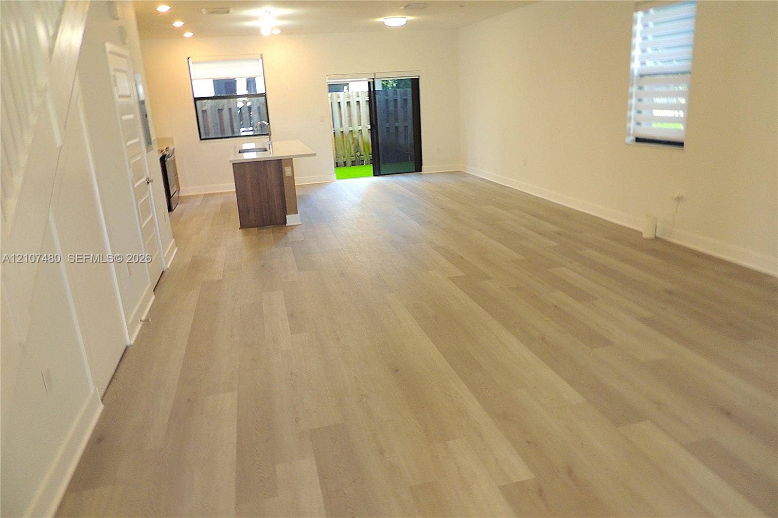 Open-concept floor plan featuring wood-finish flooring, recessed lighting, a center island with countertop seating, and sliding glass doors
