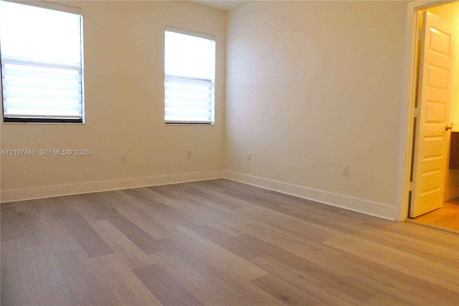Room featuring wood-finish flooring, two windows with horizontal blinds, and a multi-panel interior door