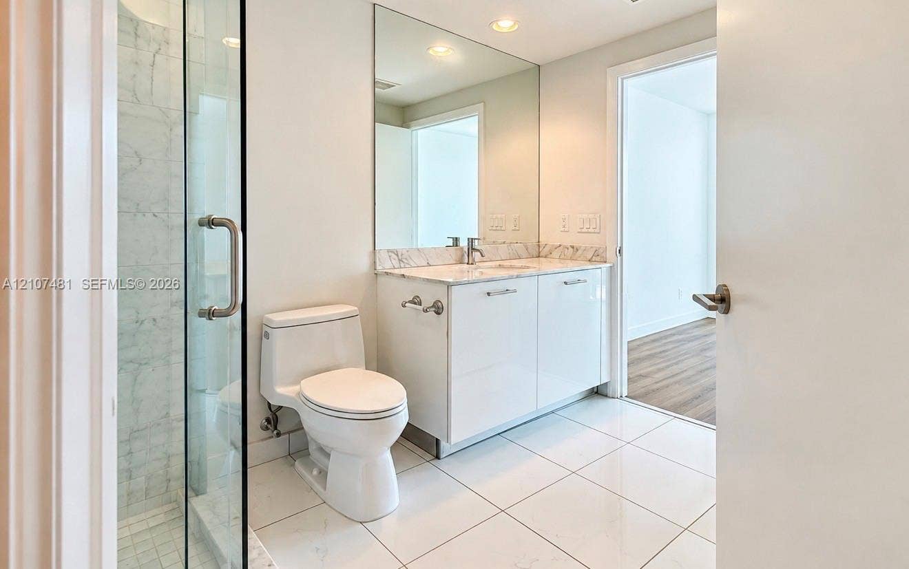 55 SE 6th Street, #2802, Miami, FL 33131 Bathroom featuring a glass-enclosed shower, stone-finish countertop, white cabinetry, wall-to-wall vanity mirror, and large-format tile flooring