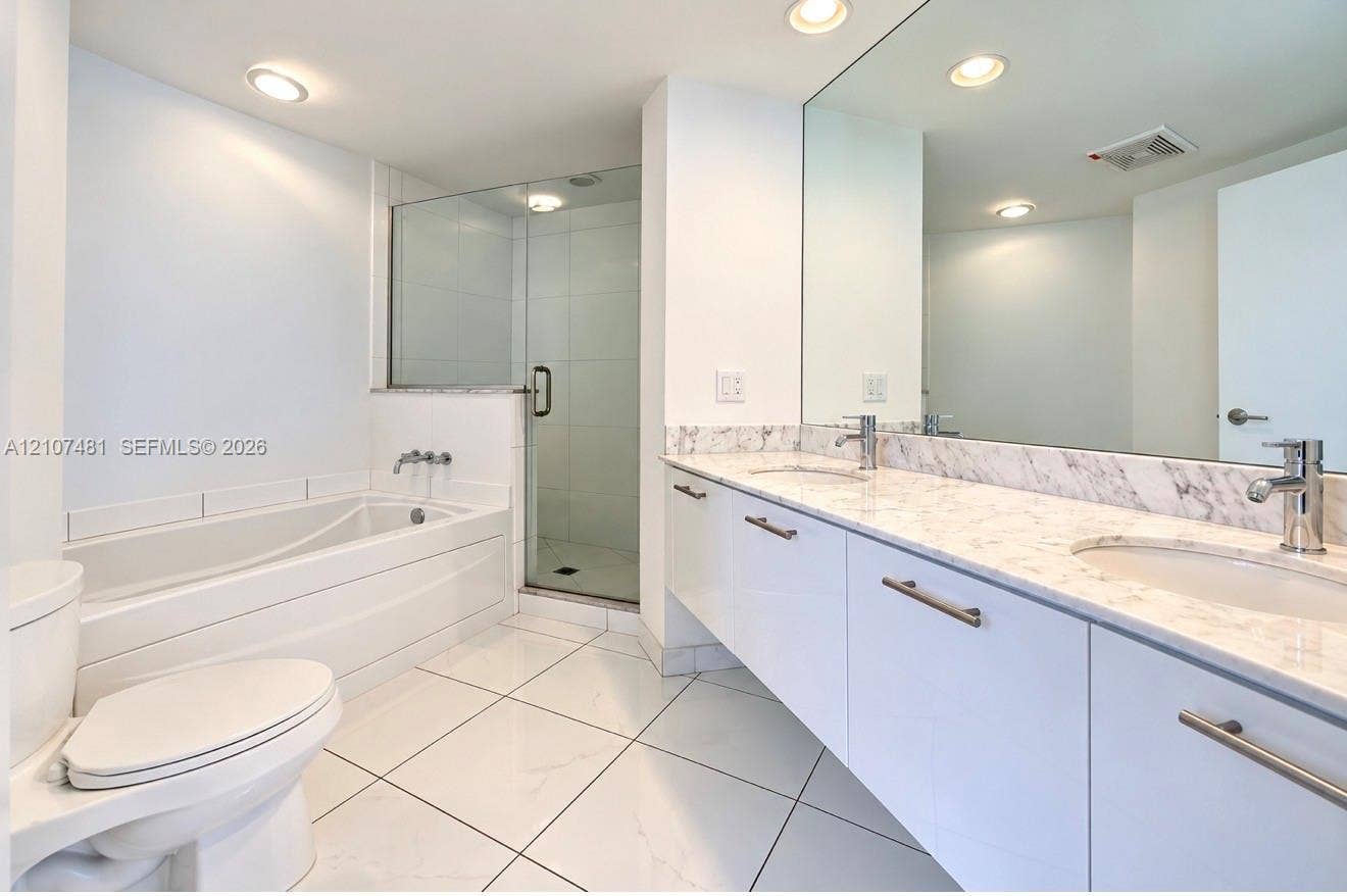 55 SE 6th Street, #2802, Miami, FL 33131 Floating vanity with dual rectangular undermount sinks, stone-finish countertops, glass-enclosed shower, deep soaking tub, and polished tile flooring