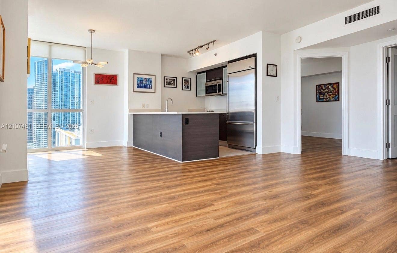 55 SE 6th Street, #2802, Miami, FL 33131 Open-concept kitchen featuring dark wood-finish cabinetry, stainless steel appliances, and a central island with a solid-surface countertop, complemented by wood-finish flooring and floor-to-ceiling windows