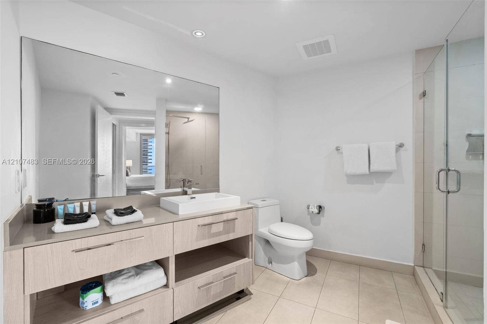 4111 S Ocean Drive, #2407, Hollywood, FL 33019 Modern bathroom featuring a wood-finish vanity with a rectangular vessel sink, quartz countertop, large wall-mounted mirror, and a glass-enclosed shower with tiled walls