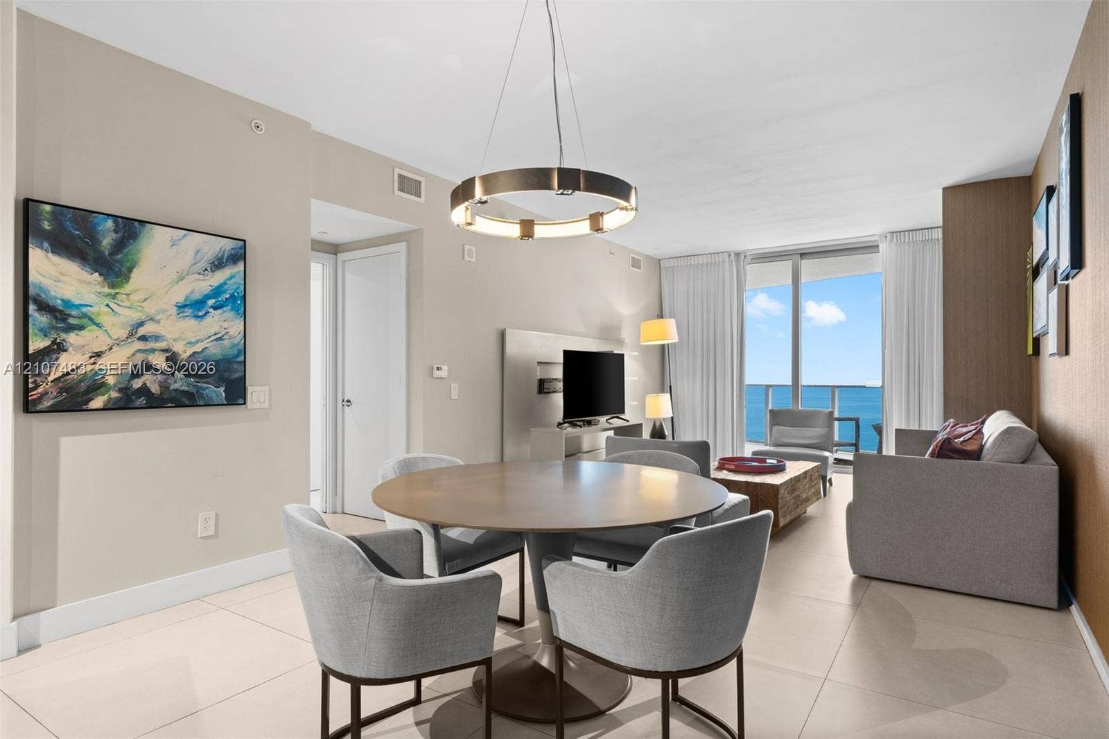 4111 S Ocean Drive, #2407, Hollywood, FL 33019 Large format neutral tile flooring, circular modern pendant lighting, and floor-to-ceiling glass sliding doors opening to a balcony with ocean scenery