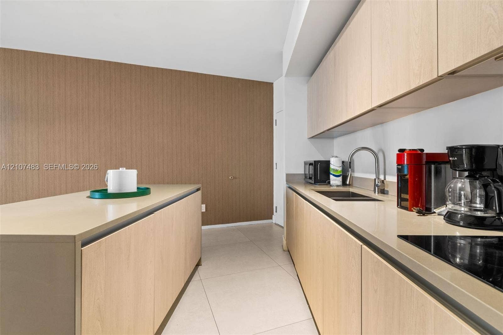 4111 S Ocean Drive, #2407, Hollywood, FL 33019 Contemporary kitchen featuring light wood-finish cabinetry, sleek solid-surface countertops, an undermount stainless steel sink, a smooth-top cooktop, and large-format tile flooring