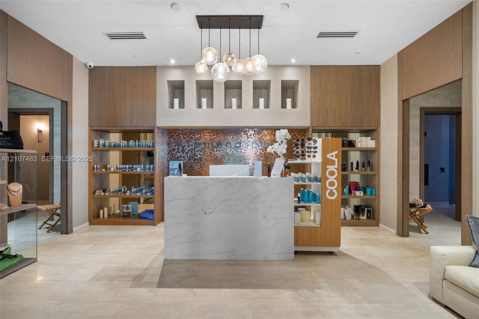4111 S Ocean Drive, #2407, Hollywood, FL 33019 Reception area featuring a stone-finish reception desk, metallic mosaic tile accent wall, built-in recessed wood-tone shelving, and custom multi-globe pendant lighting