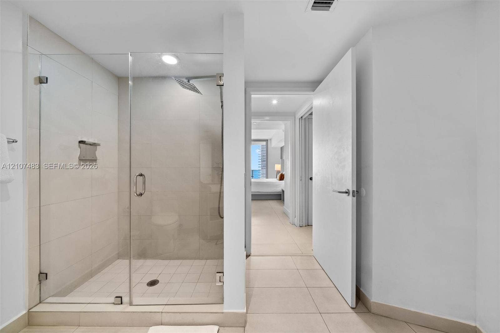 4111 S Ocean Drive, #2407, Hollywood, FL 33019 Walk-in shower featuring a glass enclosure, large-format tile surround, rainfall shower head, and built-in metal shelving, complemented by light-toned tile flooring