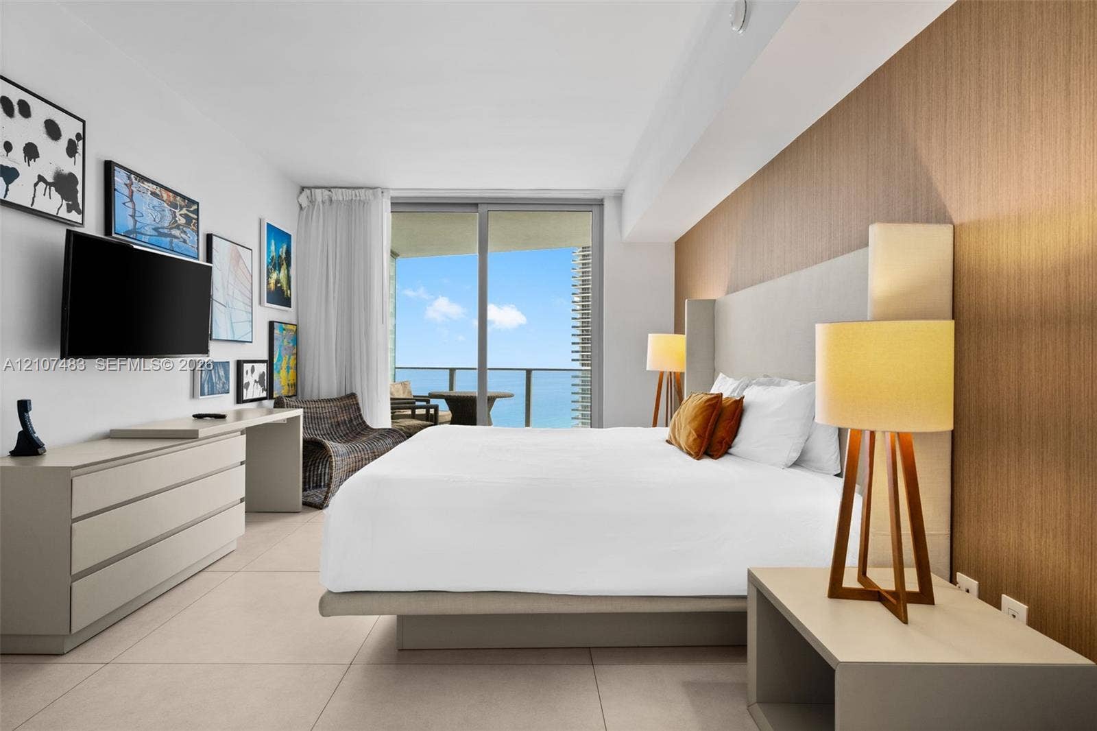 4111 S Ocean Drive, #2407, Hollywood, FL 33019 Floor-to-ceiling glass sliding doors opening to an exterior balcony, wood-finish accent wall paneling, large-format tile flooring, and custom built-in cabinetry