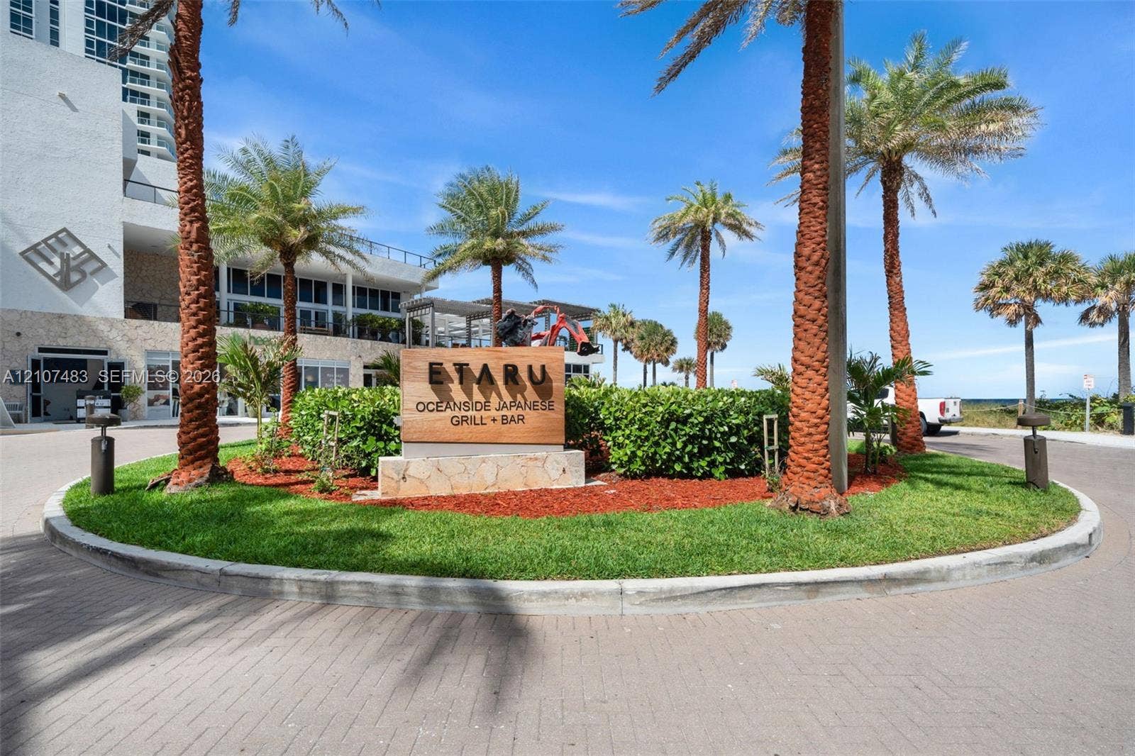 4111 S Ocean Drive, #2407, Hollywood, FL 33019 Circular paved entryway featuring mature palm trees, manicured landscaping, and natural stone signage