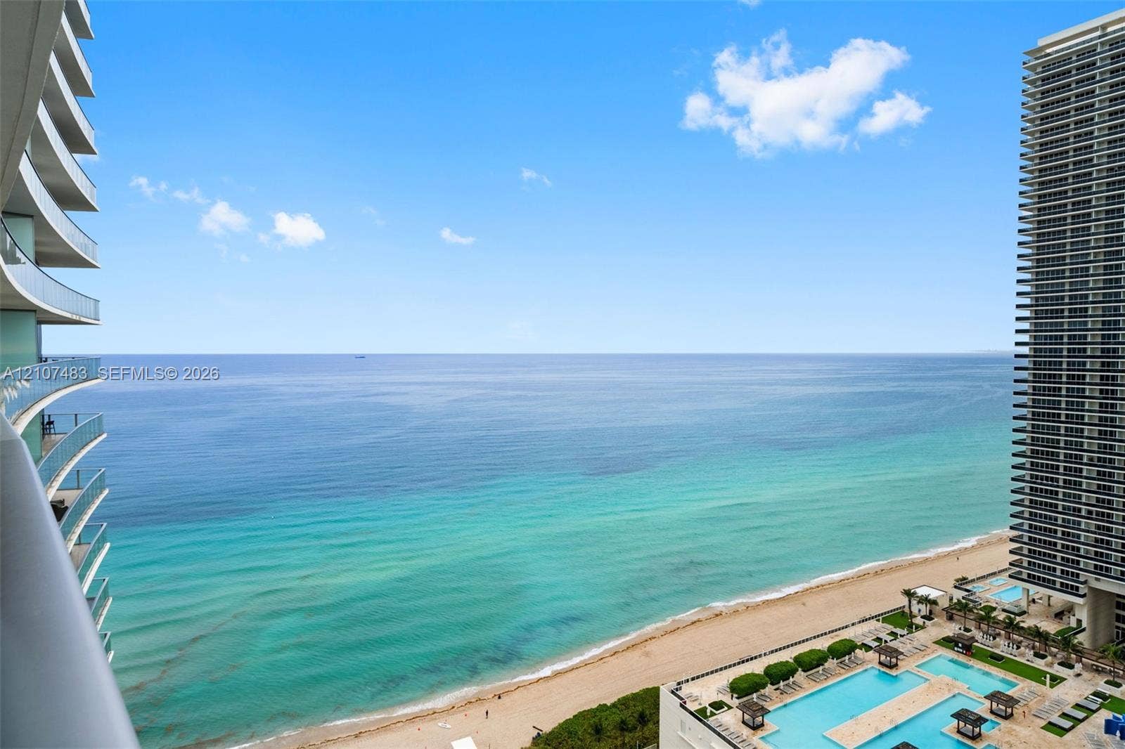 4111 S Ocean Drive, #2407, Hollywood, FL 33019 Private balcony featuring glass railings, overlooking the coastline, sandy beach, and multi-level outdoor swimming pools