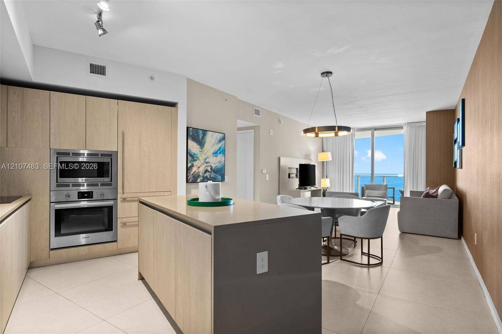 4111 S Ocean Drive, #2407, Hollywood, FL 33019 Open-concept kitchen featuring light wood-finish cabinetry, a central island with a solid surface countertop, built-in stainless steel double wall ovens, and large-format tile flooring