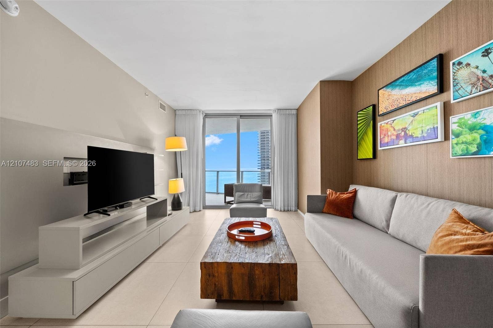 4111 S Ocean Drive, #2407, Hollywood, FL 33019 Living space featuring floor-to-ceiling sliding glass doors, neutral tile flooring, a custom wood-paneled accent wall, and a built-in media console