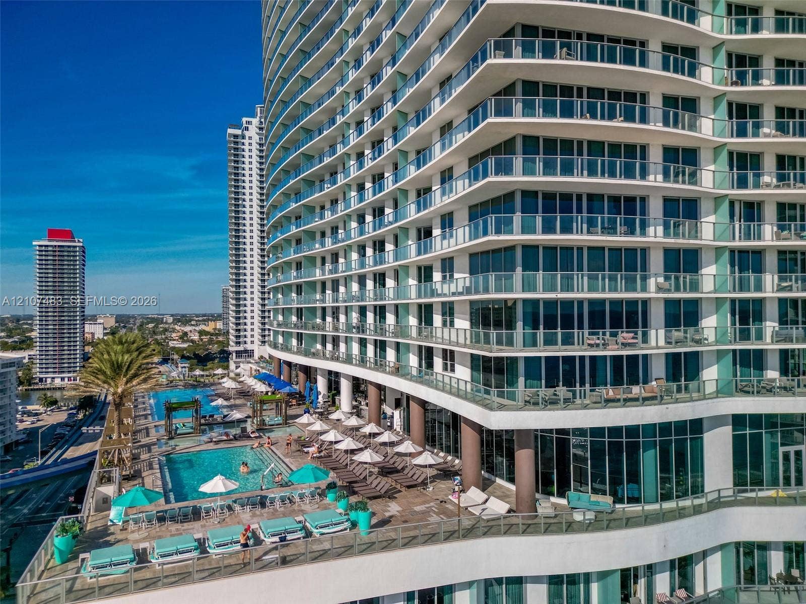 4111 S Ocean Drive, #2407, Hollywood, FL 33019 High-rise architecture featuring tiered, wrap-around glass balconies, expansive floor-to-ceiling windows, and a multi-level pool deck with built-in stone hardscaping