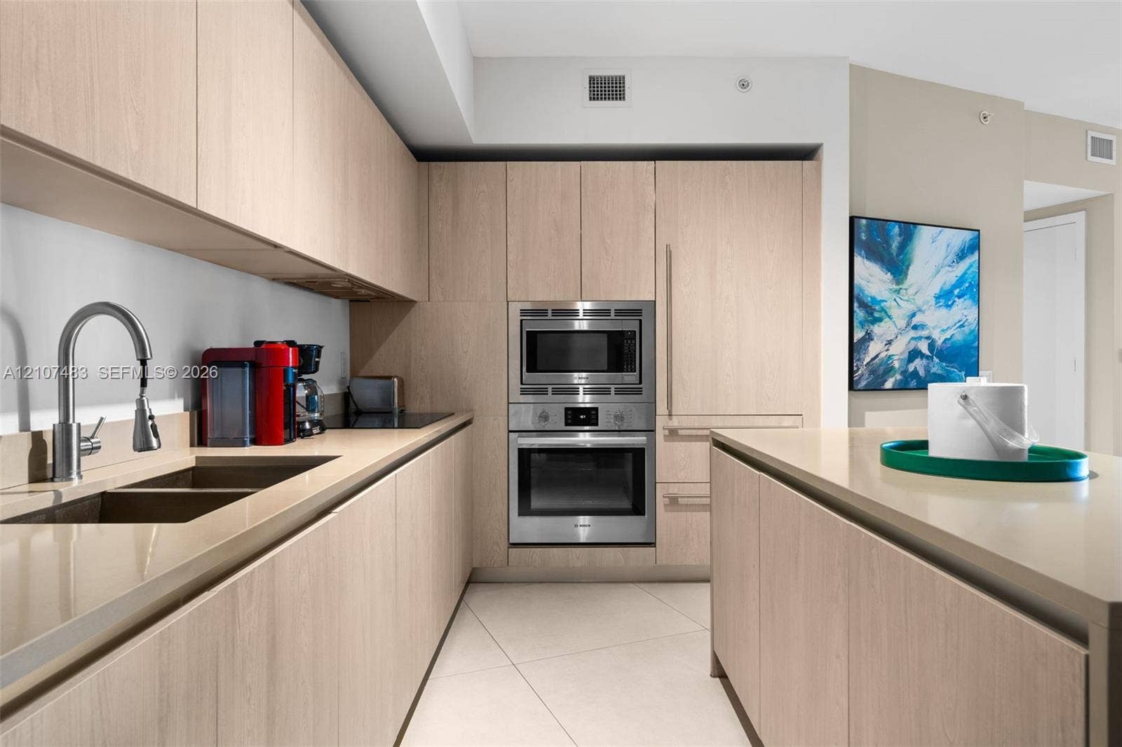 4111 S Ocean Drive, #2407, Hollywood, FL 33019 Kitchen featuring light-finish wood cabinetry, integrated stainless steel oven and microwave, stone-finish countertops, and an undermount dual-basin sink with a high-arch faucet