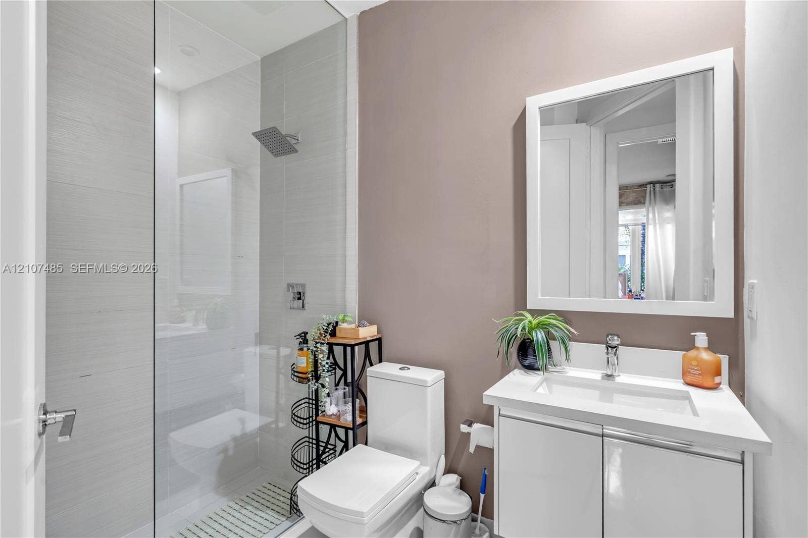 10545 NW 63rd Terrace, Doral, FL 33178 Bathroom featuring a glass-enclosed shower with horizontal wall tile, rainfall showerhead, white vanity with an integrated rectangular sink, and a framed wall mirror