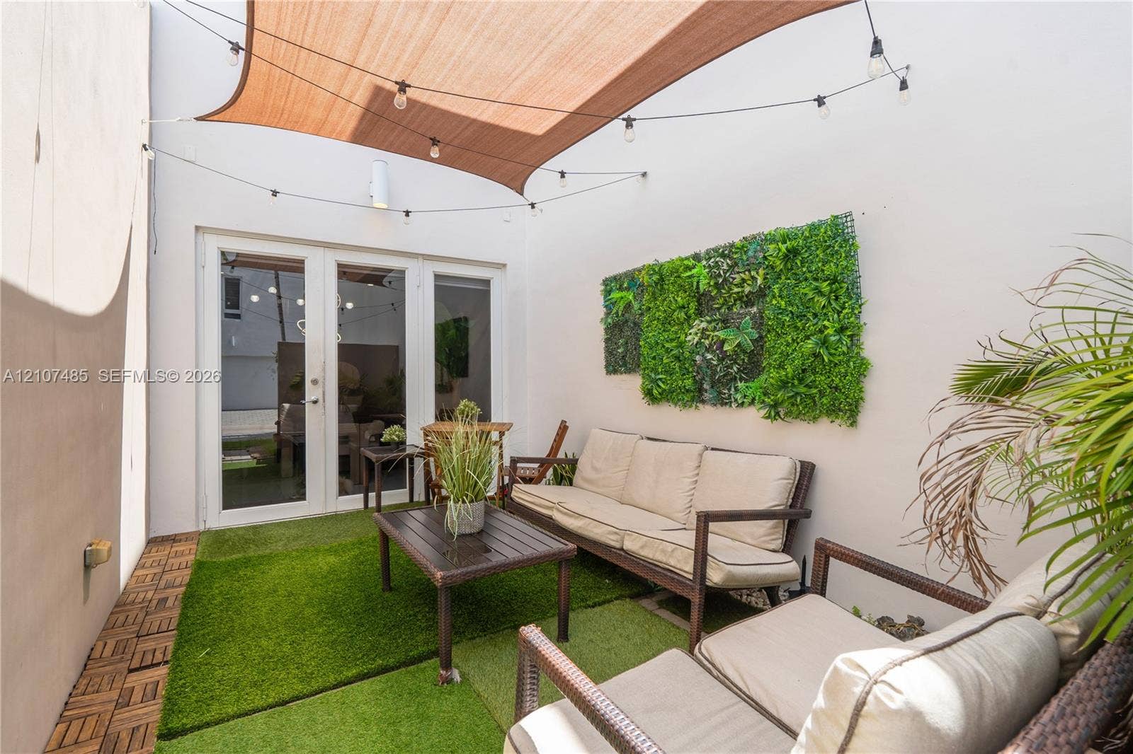10545 NW 63rd Terrace, Doral, FL 33178 Enclosed patio area featuring white stucco walls, synthetic turf surfacing, a retractable fabric shade canopy, integrated string lighting, and a wall-mounted artificial vertical garden