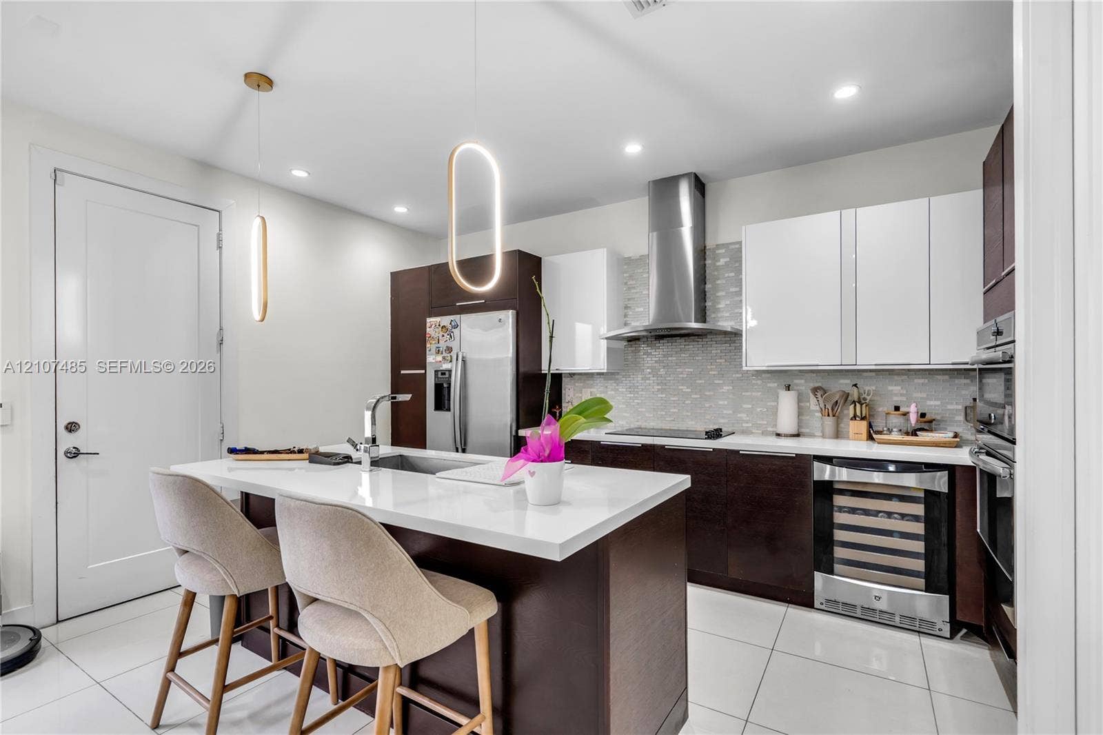 10545 NW 63rd Terrace, Doral, FL 33178 Kitchen featuring two-tone cabinetry, quartz countertops, a central island with an undermount sink, built-in wine cooler, and stainless steel range hood