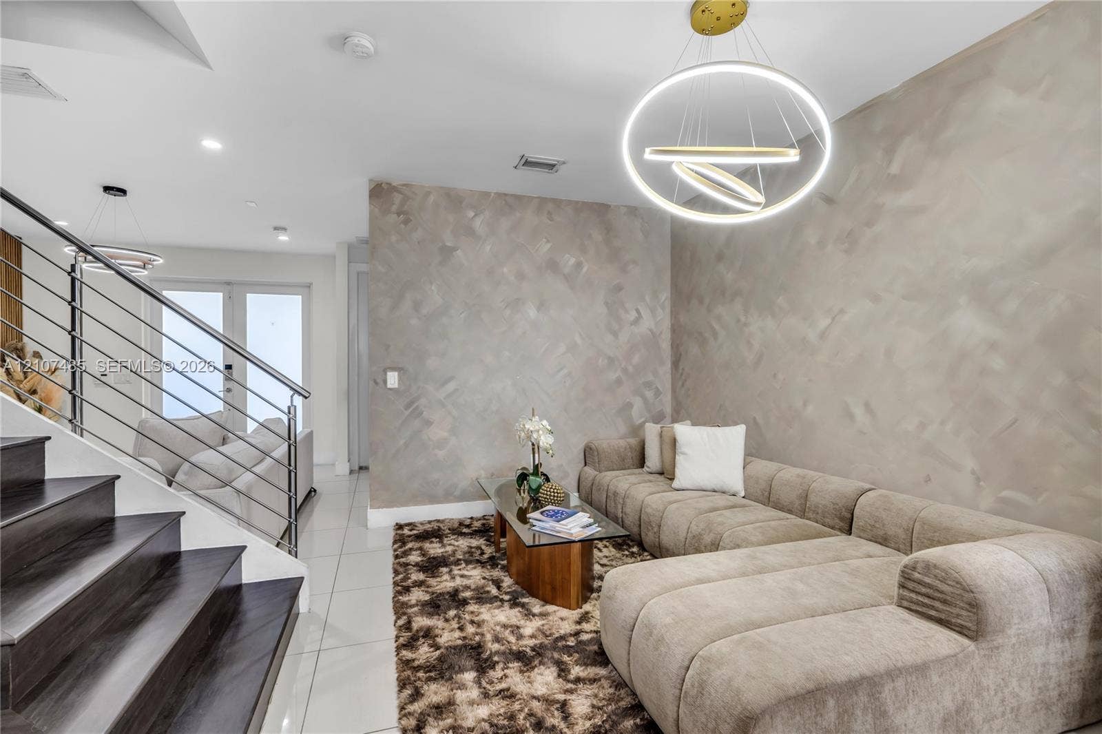 10545 NW 63rd Terrace, Doral, FL 33178 Staircase featuring wood-finish treads and a horizontal cable railing system, polished large-format tile flooring, textured accent wall, and a contemporary multi-ring pendant light fixture