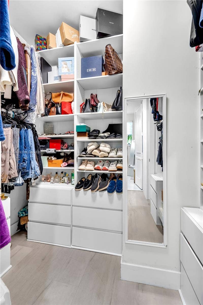 10545 NW 63rd Terrace, Doral, FL 33178 Walk-in closet featuring white custom built-in shelving, floor-to-ceiling storage units, multiple integrated drawer banks, and light-toned wood-finish flooring