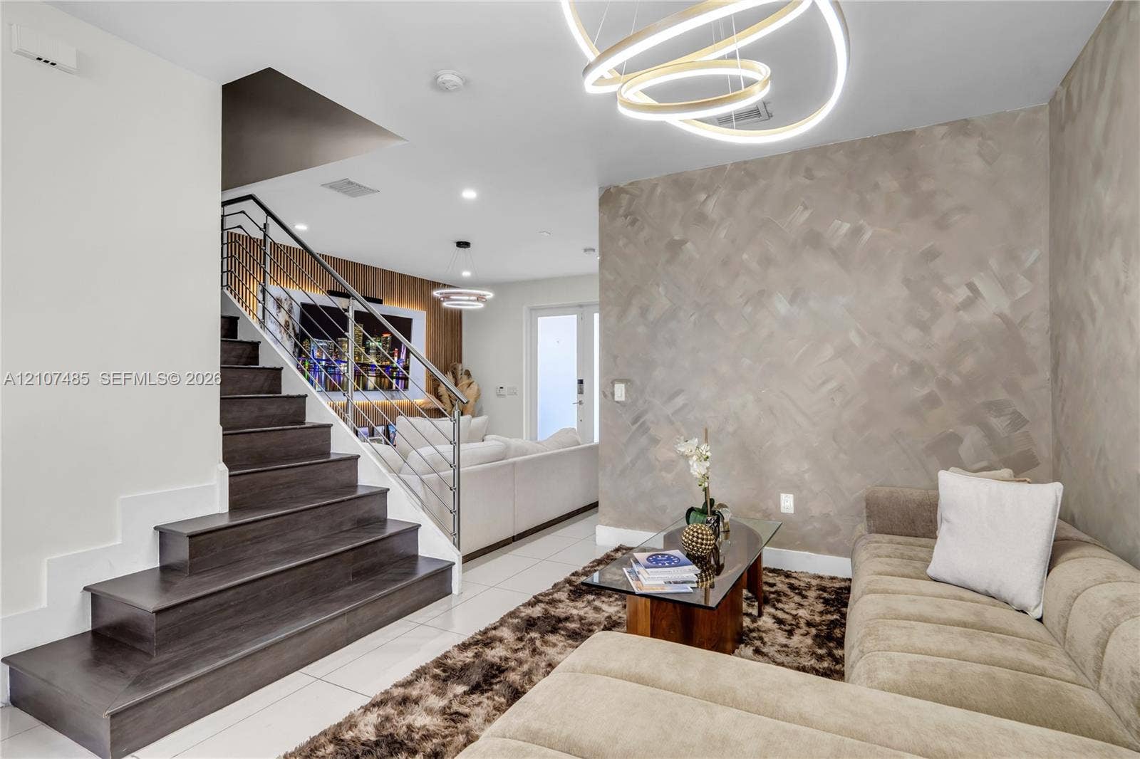 10545 NW 63rd Terrace, Doral, FL 33178 Staircase with dark wood-finish treads and metal cable railings, custom textural accent wall, circular LED chandelier, and polished tile flooring