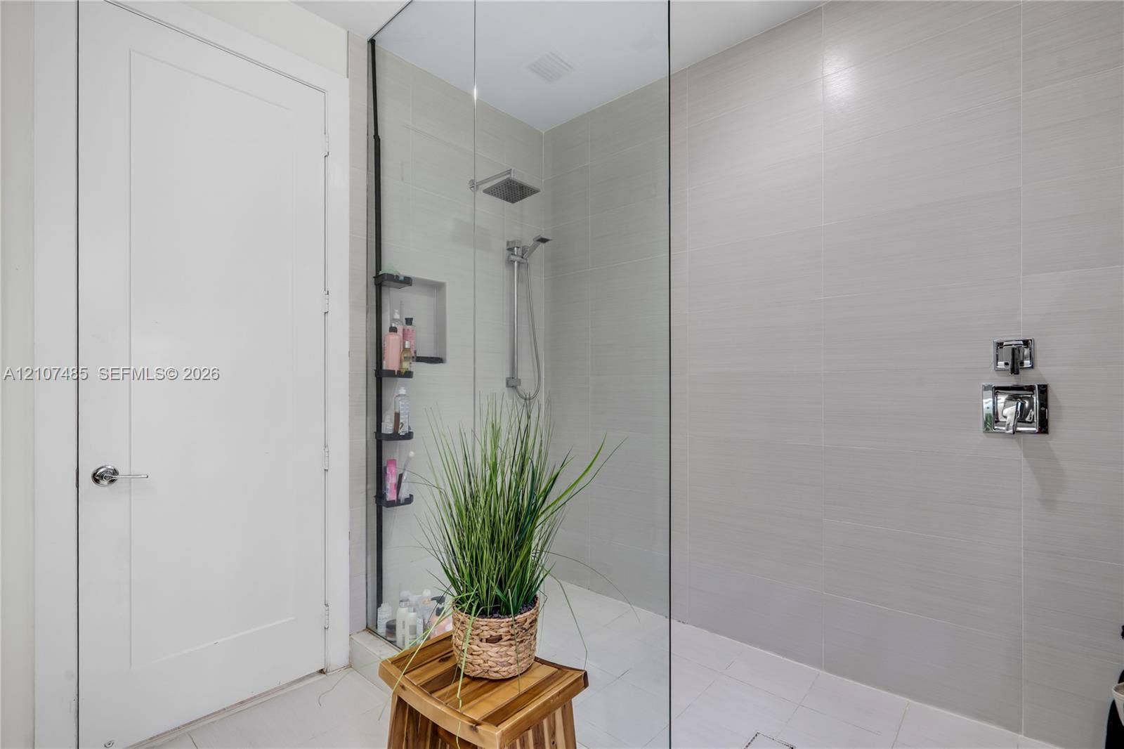 10545 NW 63rd Terrace, Doral, FL 33178 Walk-in shower featuring floor-to-ceiling ceramic tile, frameless glass enclosure, built-in recessed storage niche, and polished chrome rainfall showerhead with handheld attachment
