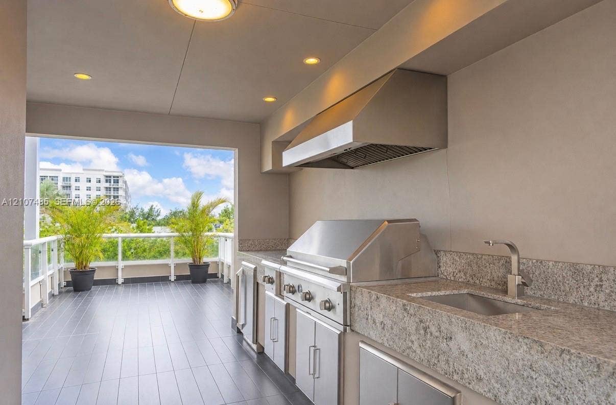 10545 NW 63rd Terrace, Doral, FL 33178 Outdoor kitchen featuring stainless steel built-in grill, stone-finish countertop, undermount sink, professional-grade range hood, and tile flooring