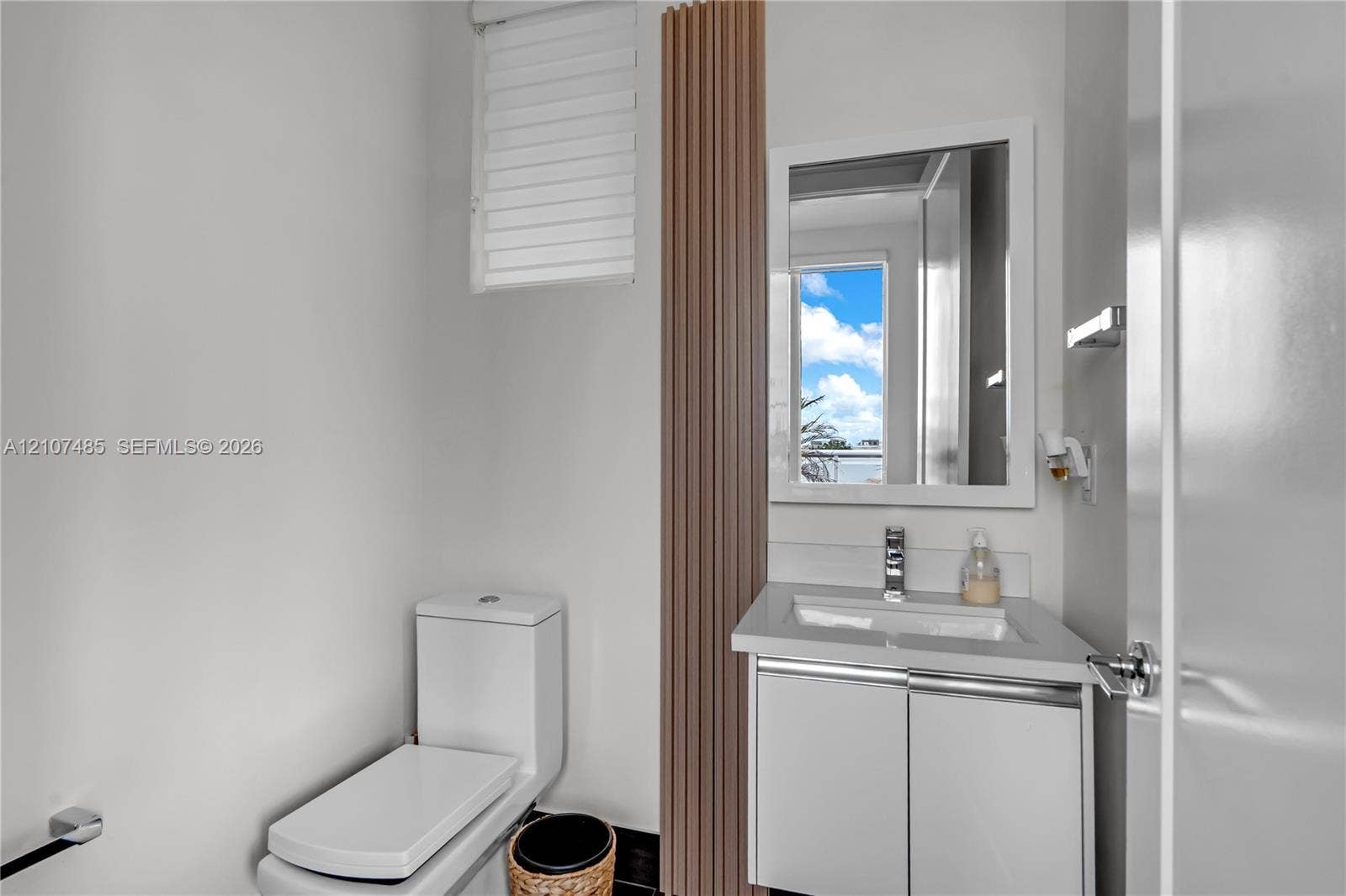 10545 NW 63rd Terrace, Doral, FL 33178 Compact vanity with stone-composite countertop, undermount sink, chrome faucet, vertical wood-slat accent panel, and wall-mounted mirror