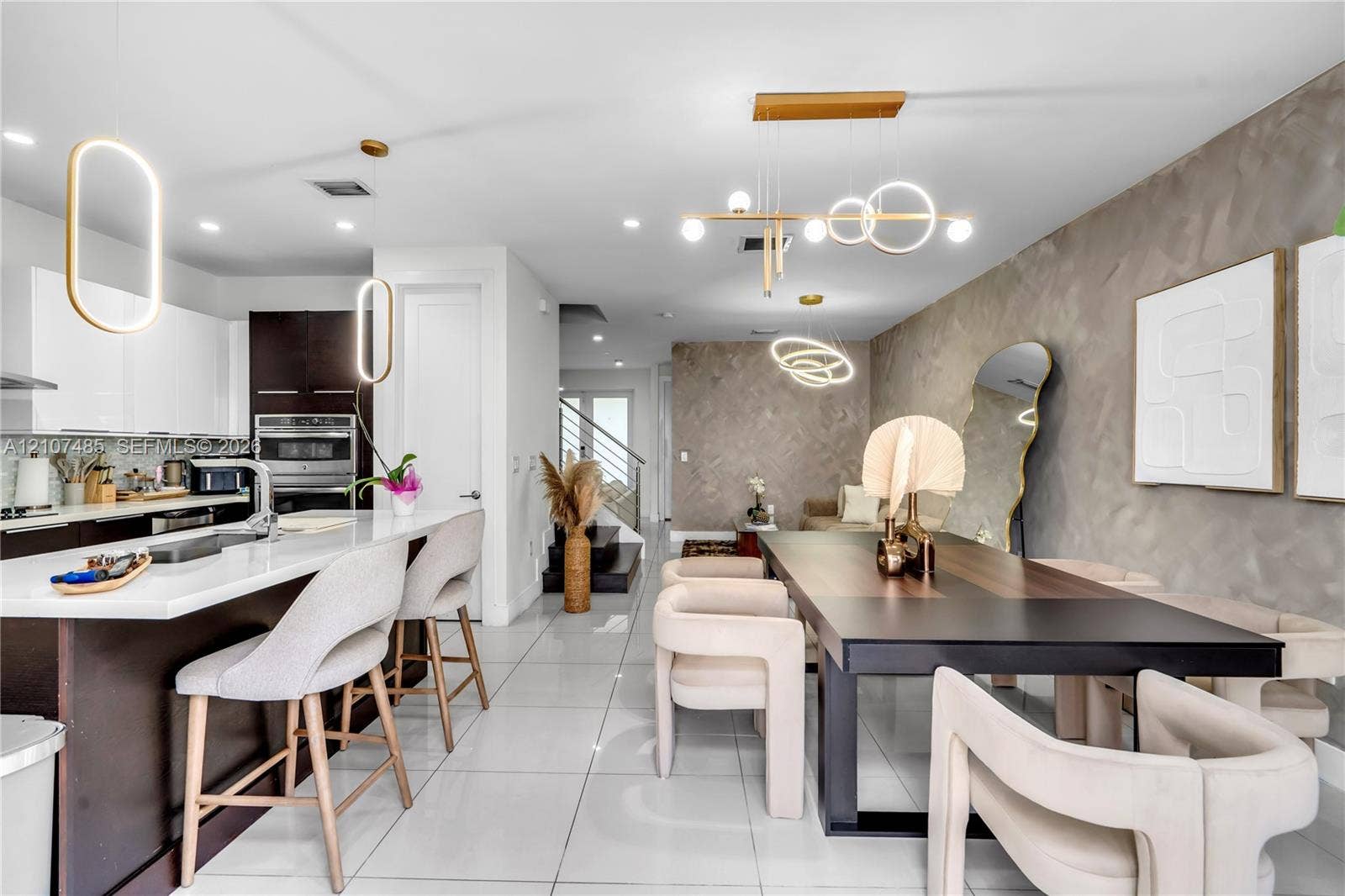 10545 NW 63rd Terrace, Doral, FL 33178 Open-concept kitchen featuring high-gloss cabinetry, a spacious island with a stone-finish countertop, large-format tile flooring, textured accent walls, and custom modern pendant lighting