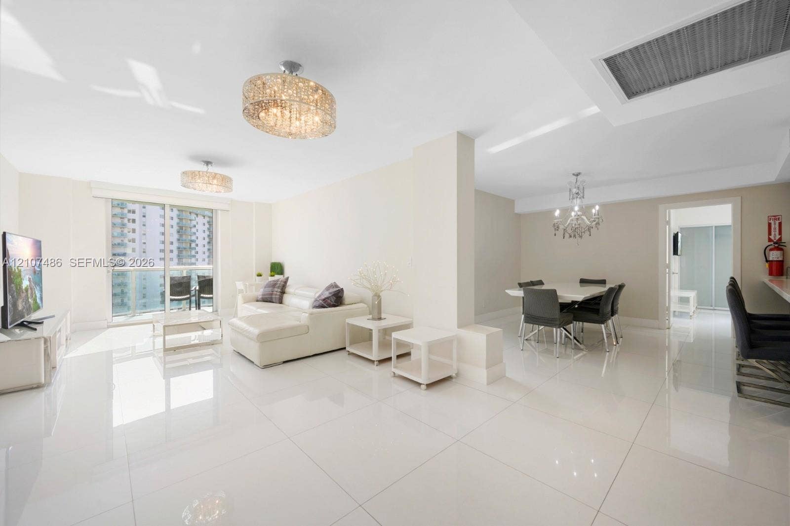 19370 Collins Avenue, #916, Sunny Isles Beach, Sunny Isles Beach, FL 33160 Open-concept living space featuring high-gloss tile flooring, dual contemporary crystal drum chandeliers, a glass-encased crystal dining chandelier, and sliding glass doors leading to a balcony