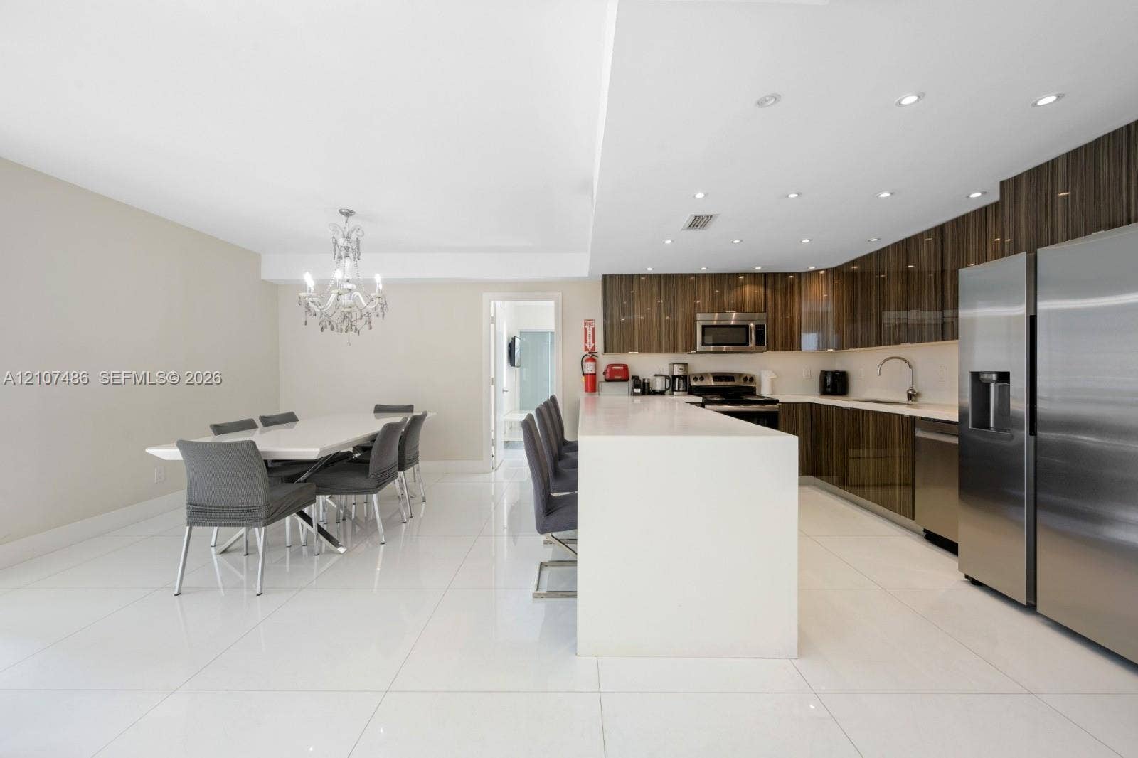 19370 Collins Avenue, #916, Sunny Isles Beach, Sunny Isles Beach, FL 33160 Kitchen featuring high-gloss cabinetry, stone-surface breakfast bar, polished tile flooring, stainless steel appliances, and crystal chandelier lighting