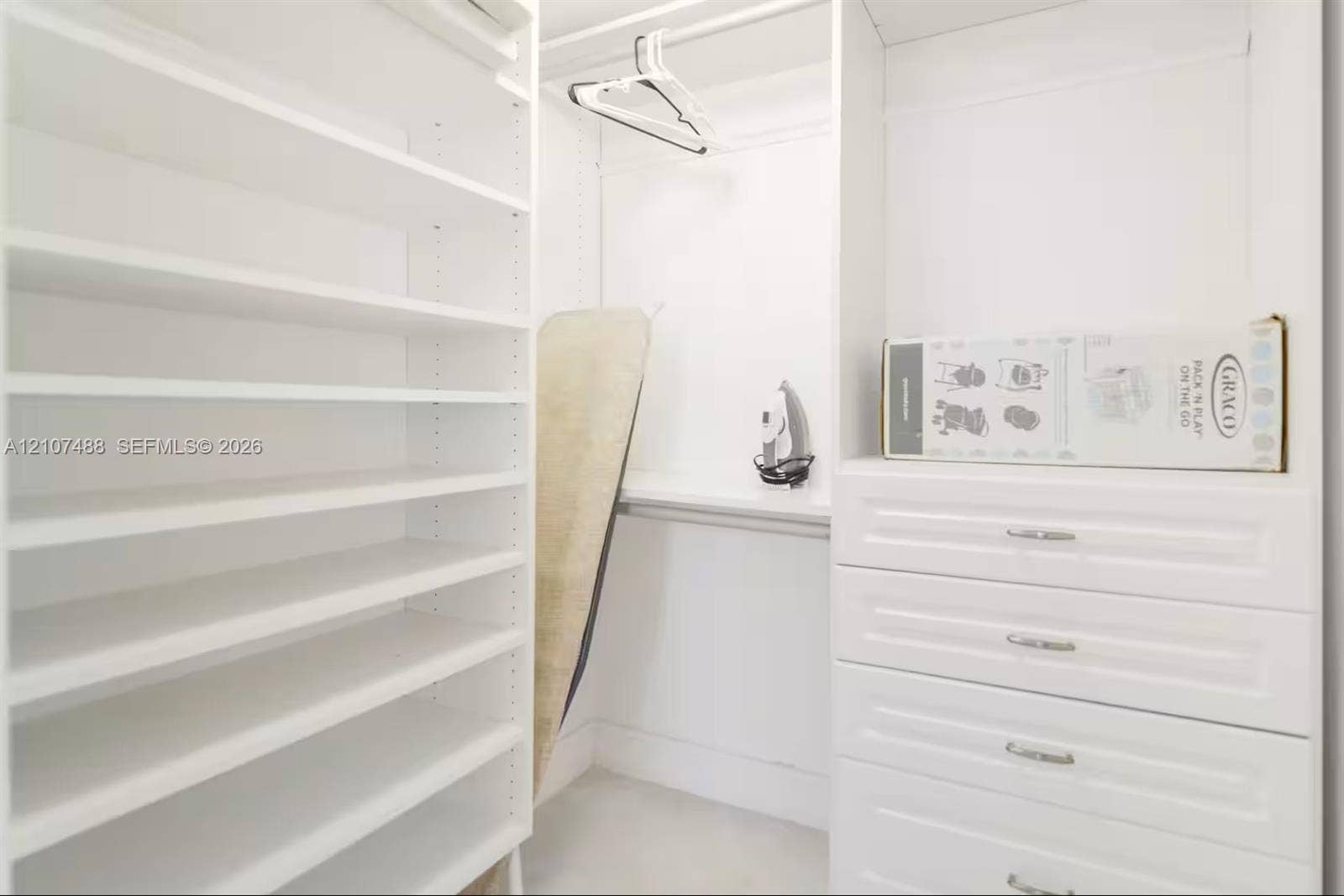 Custom built-in closet featuring white cabinetry, floor-to-ceiling adjustable shelving, integrated storage drawers with metal hardware, and overhead hanging rods