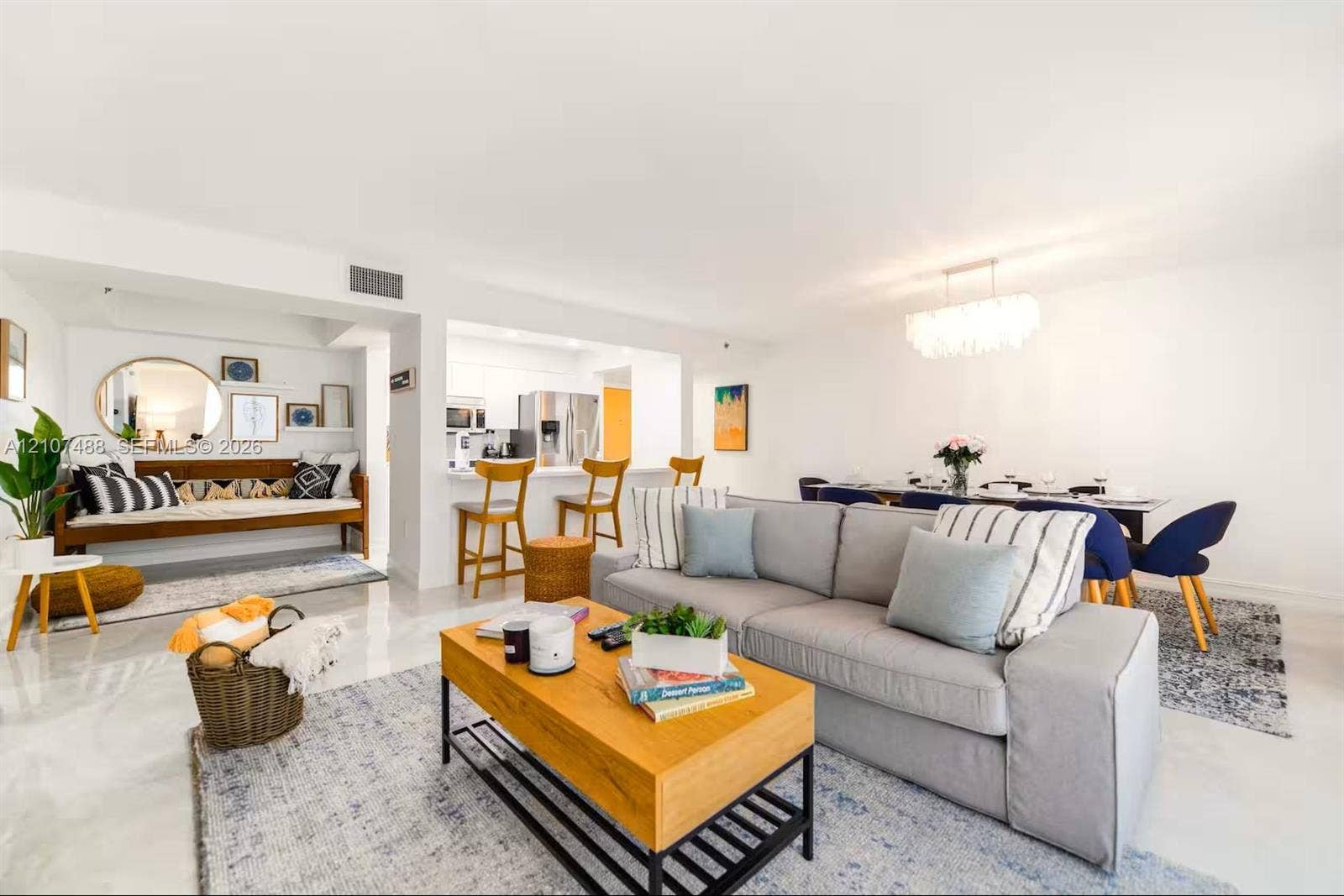 Open-concept living space featuring high-gloss tile flooring, white cabinetry, a built-in kitchen breakfast bar, and an integrated chandelier light fixture