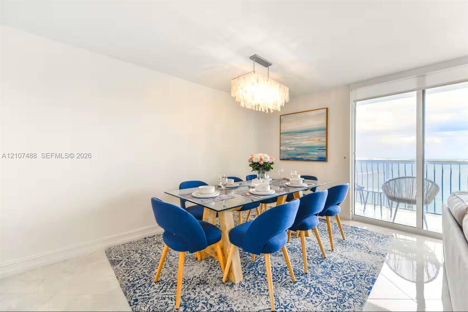 Dining area featuring polished tile flooring, a tiered crystal-style chandelier, and floor-to-ceiling glass sliding doors opening to a balcony
