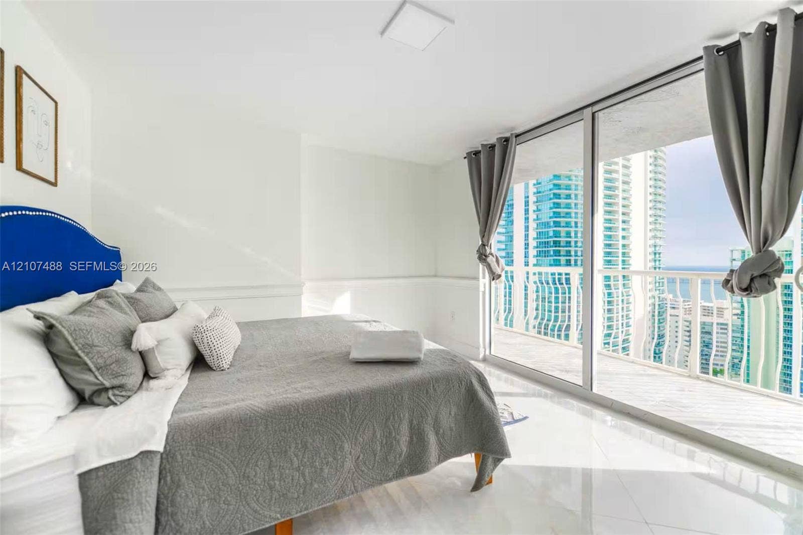 Floor-to-ceiling sliding glass doors, white tile flooring, and a private balcony featuring a metal railing