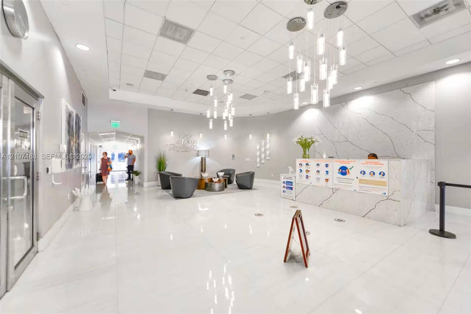 Lobby featuring high-gloss tile flooring, white stone-finish reception desk with dramatic veining, and modern multi-pendant lighting fixtures