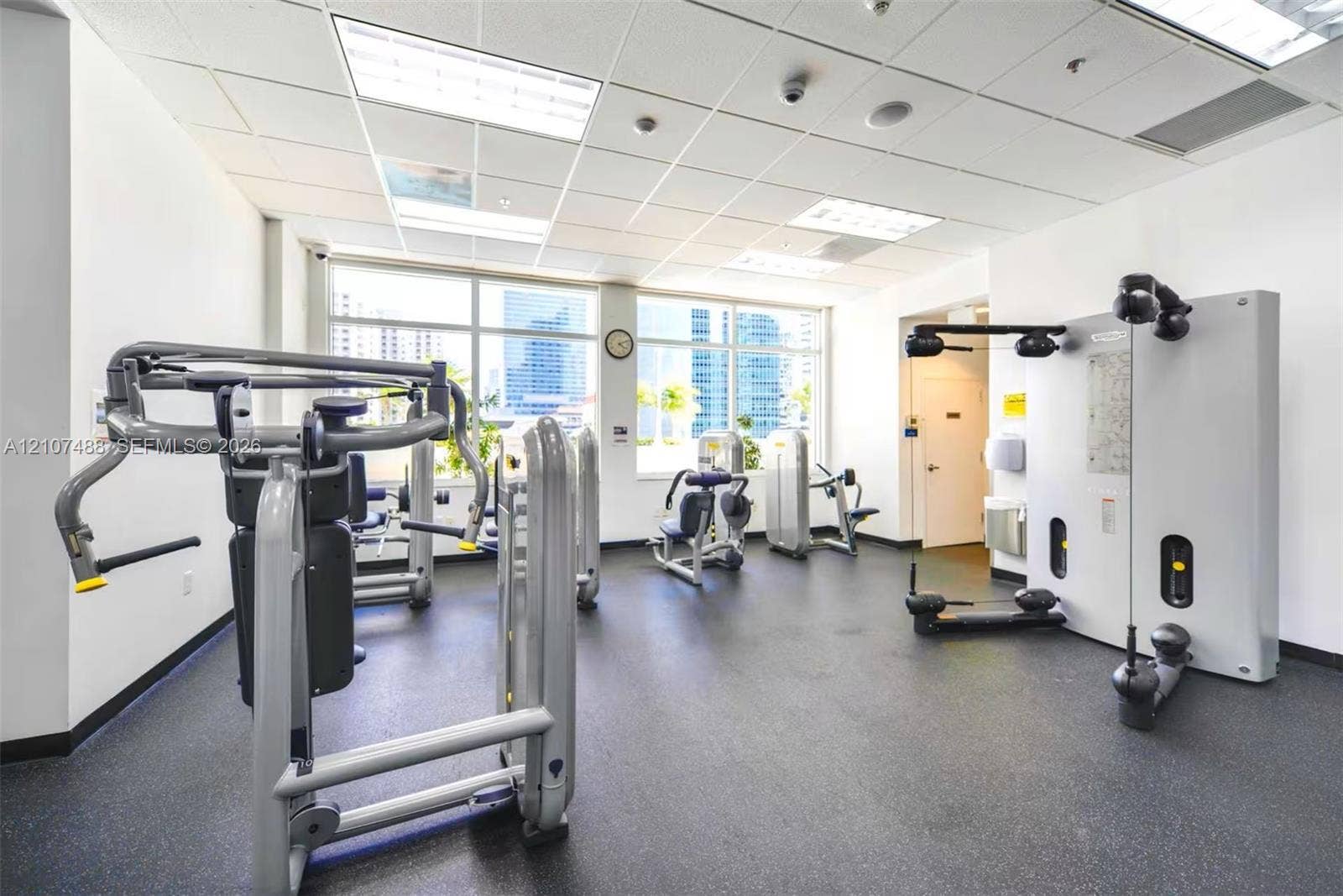 Fitness center featuring a rubberized floor surface, drop ceiling with recessed lighting, and expansive windows