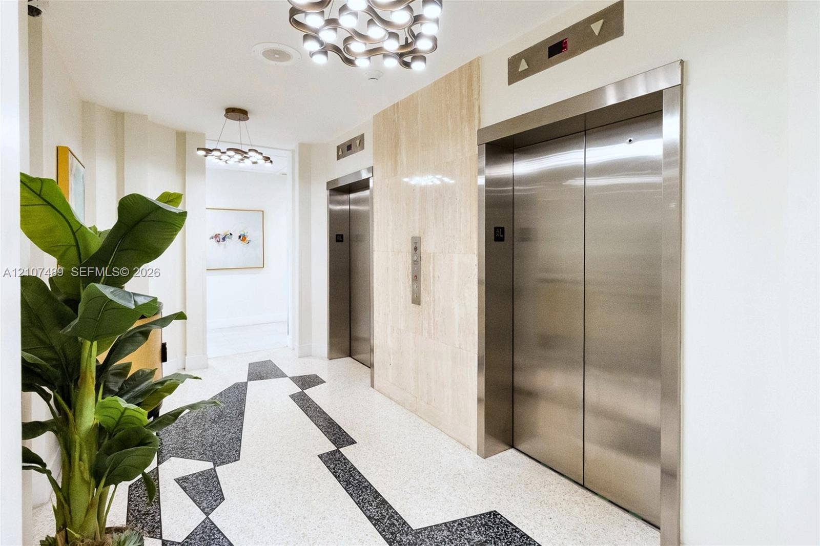 2000 S Ocean Boulevard, #9N, Lauderdale-By-The-Sea, Lauderdale By The Sea, FL 33062 Elevator foyer featuring dual brushed-metal elevator doors, neutral stone wall cladding, geometric patterned flooring, and contemporary multi-bulb ceiling lighting
