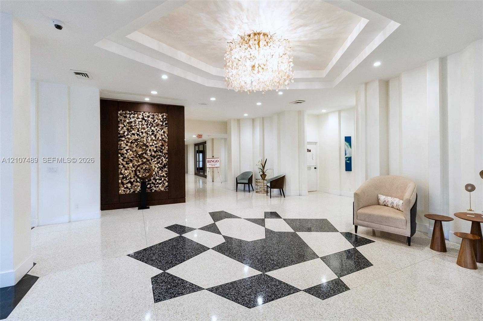 2000 S Ocean Boulevard, #9N, Lauderdale-By-The-Sea, Lauderdale By The Sea, FL 33062 Foyer featuring a recessed tray ceiling with a crystal chandelier, polished stone flooring with geometric inlay, and a dark wood-paneled accent wall