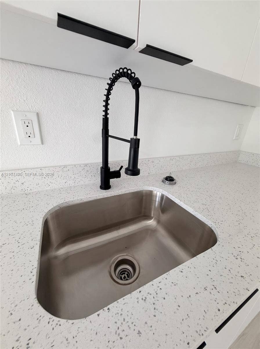 Undermount stainless steel sink featuring a matte black high-arc pull-down faucet, speckled composite countertop, and white cabinetry with matte black linear hardware