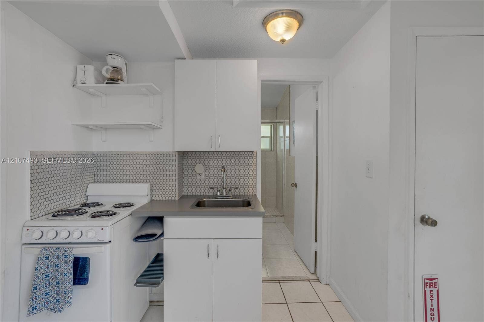 2645 NE 32nd Street, Fort Lauderdale, FL 33306 Kitchenette featuring white cabinetry, a neutral-toned countertop, a hexagonal tile backsplash, a white four-burner gas range, and a drop-in sink