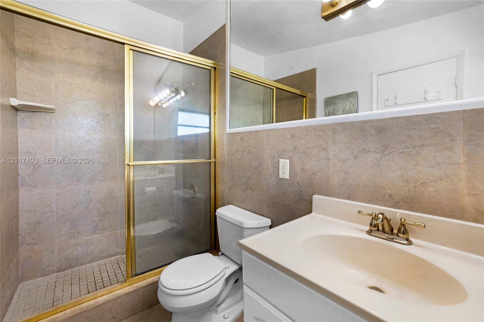 2645 NE 32nd Street, Fort Lauderdale, FL 33306 Bathroom featuring a shower stall with a glass door, tile surround, vanity with an integrated sink, and a wall-to-wall mirror