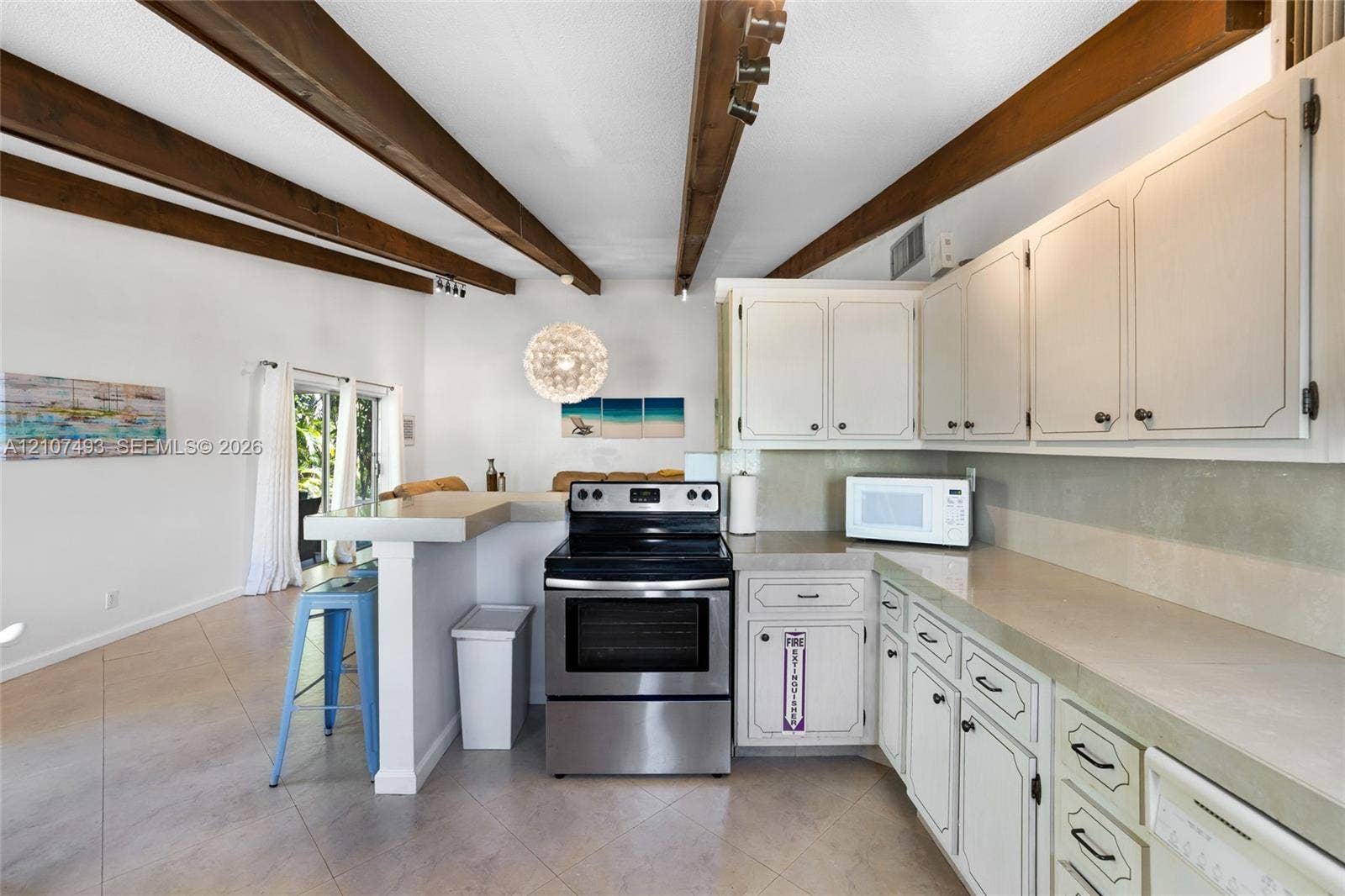 2645 NE 32nd Street, Fort Lauderdale, FL 33306 Kitchen featuring exposed wood ceiling beams, solid-surface countertops, white cabinetry, and stainless steel range