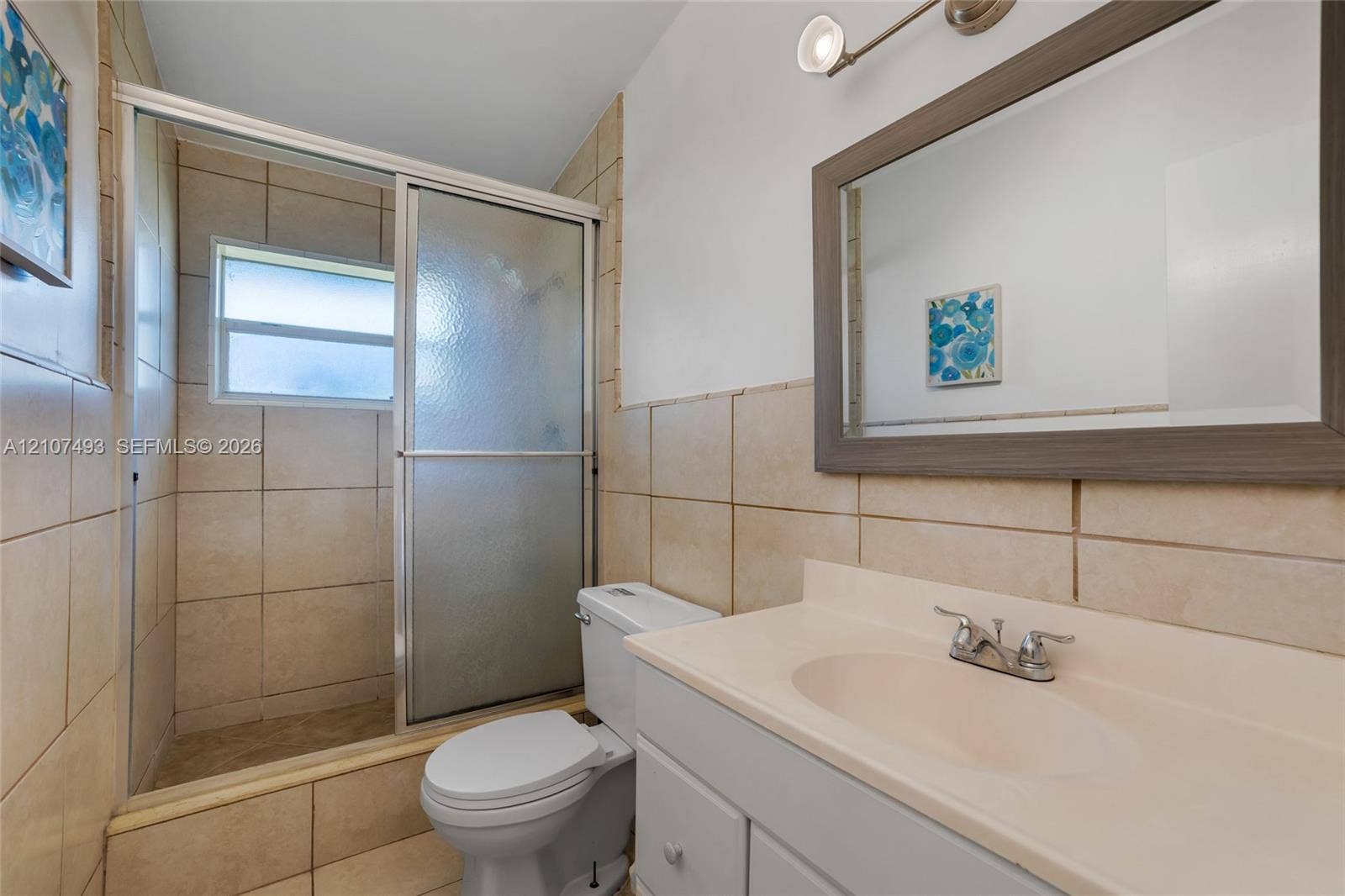 2645 NE 32nd Street, Fort Lauderdale, FL 33306 Bathroom featuring a vanity with an integrated basin, a framed wall mirror, a tiled shower enclosure with sliding glass doors, and light-toned wall tile