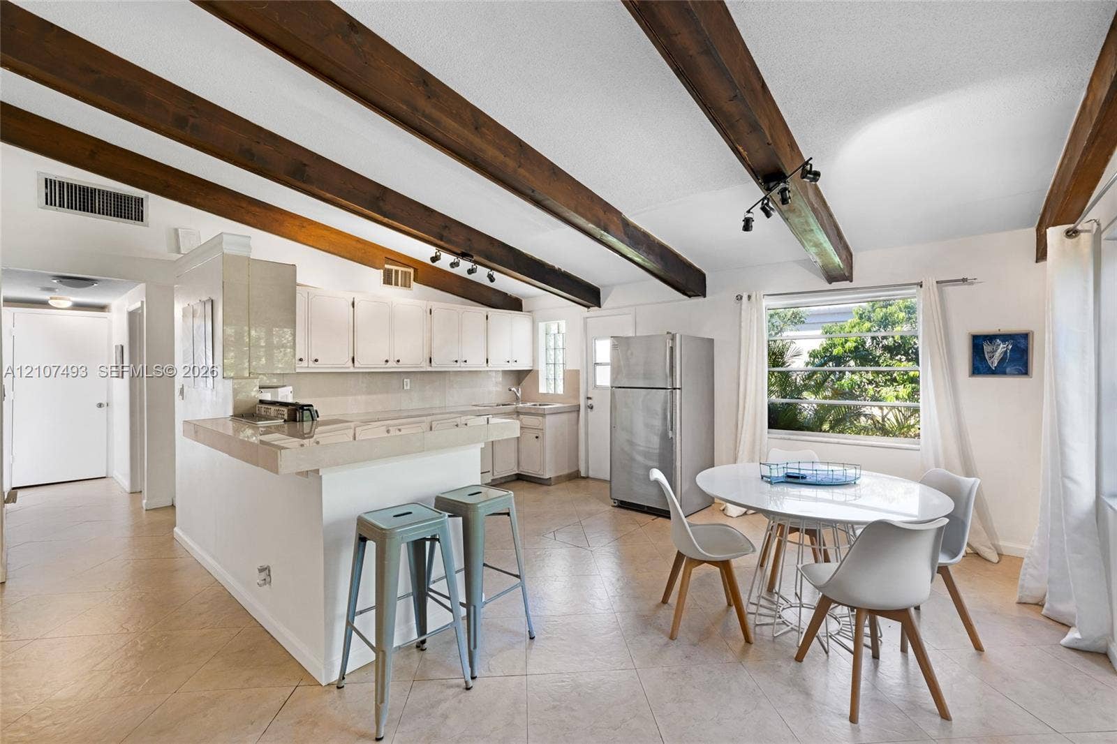 2645 NE 32nd Street, Fort Lauderdale, FL 33306 Exposed dark wood ceiling beams, tile flooring, white cabinetry, integrated peninsula, and track lighting