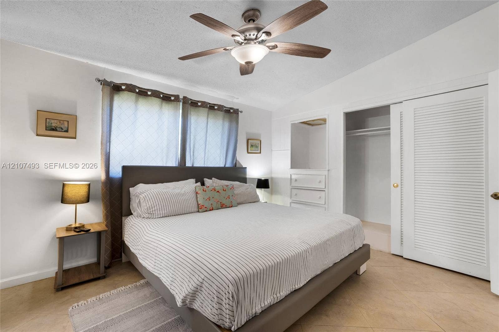 2645 NE 32nd Street, Fort Lauderdale, FL 33306 Neutral-toned tile flooring, ceiling fan with integrated lighting, built-in dresser with inset mirror, and sliding louvered closet doors
