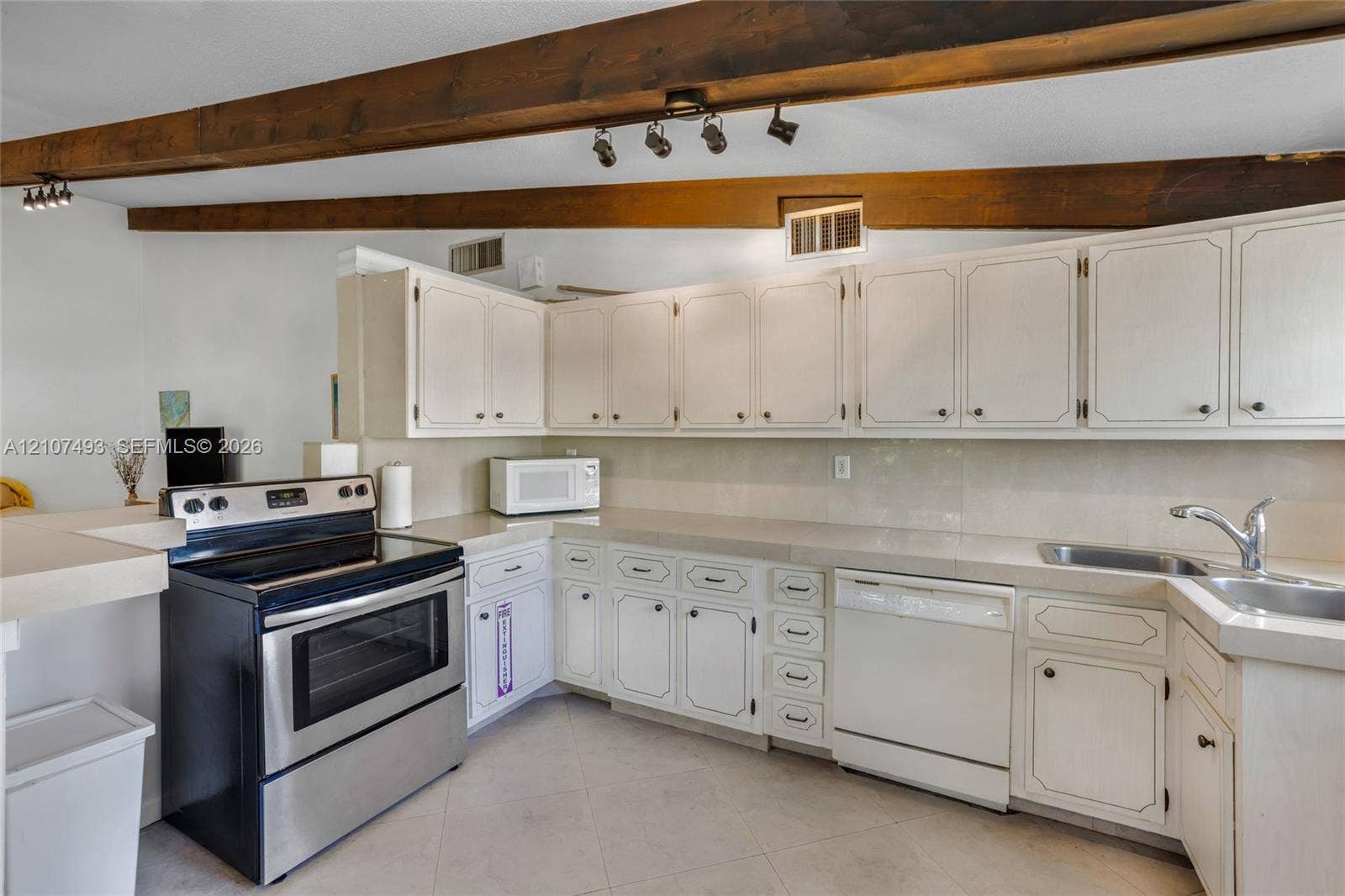 2645 NE 32nd Street, Fort Lauderdale, FL 33306 Kitchen featuring white cabinetry, solid-surface countertops, stainless steel range, integrated dishwasher, and exposed wood ceiling beams