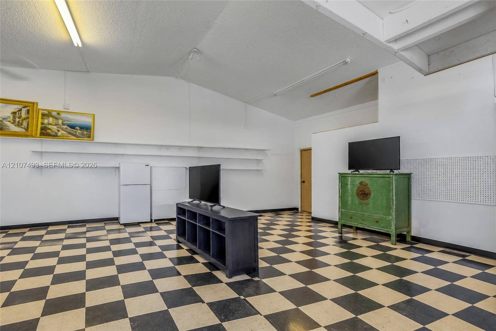 2645 NE 32nd Street, Fort Lauderdale, FL 33306 Interior space featuring vaulted ceilings, high-contrast checkerboard flooring, linear wall-mounted shelving, and integrated pegboard wall panels