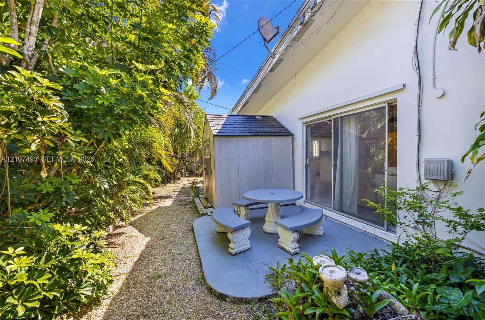 2645 NE 32nd Street, Fort Lauderdale, FL 33306 Side patio featuring a concrete slab, sliding glass door access, and a detached storage structure nestled among mature landscaping