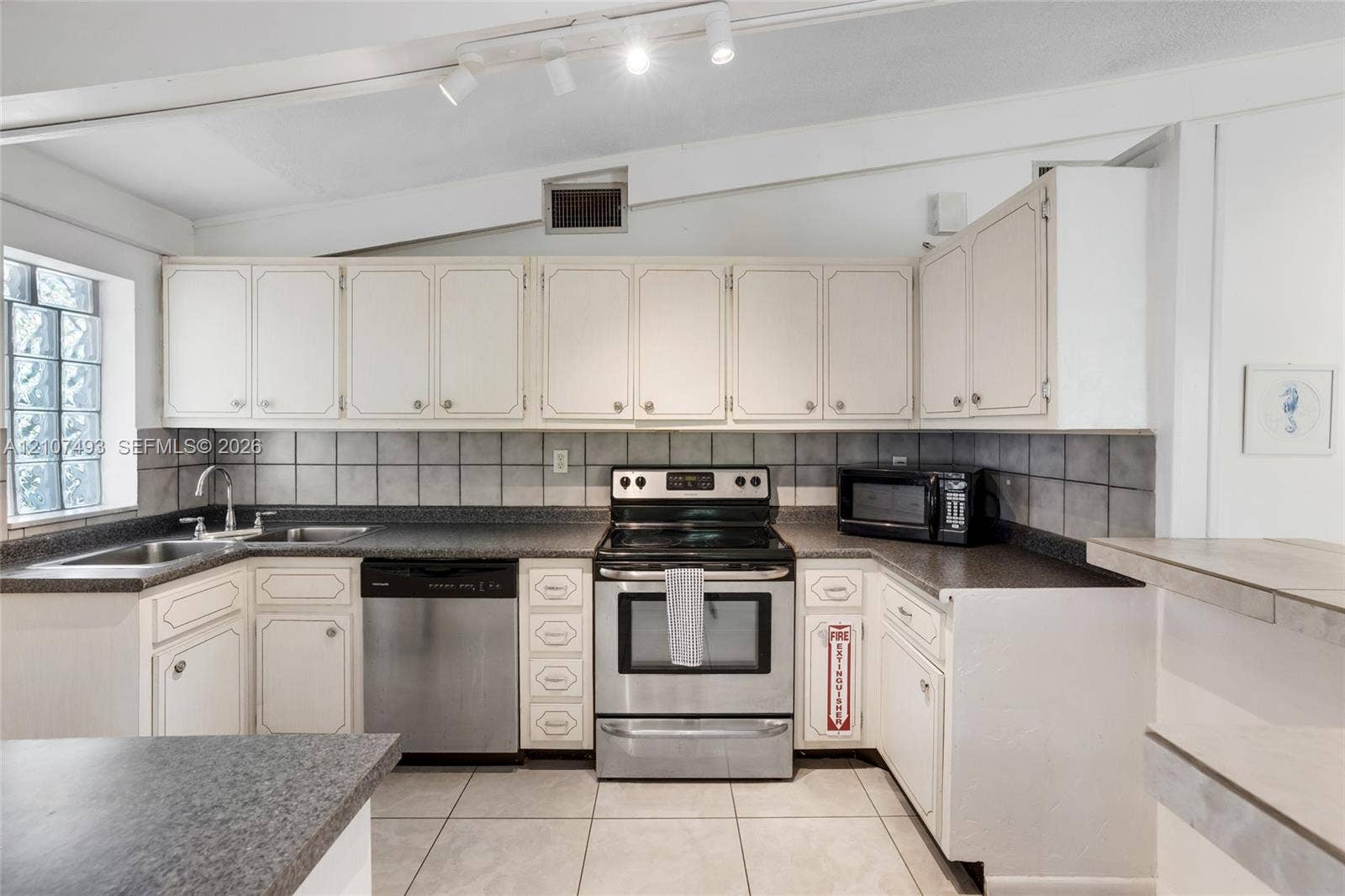 2645 NE 32nd Street, Fort Lauderdale, FL 33306 Kitchen featuring cabinetry with white shaker-style doors, stone-finish countertops, stainless steel appliances, ceramic tile backsplash, and ceramic floor tiling