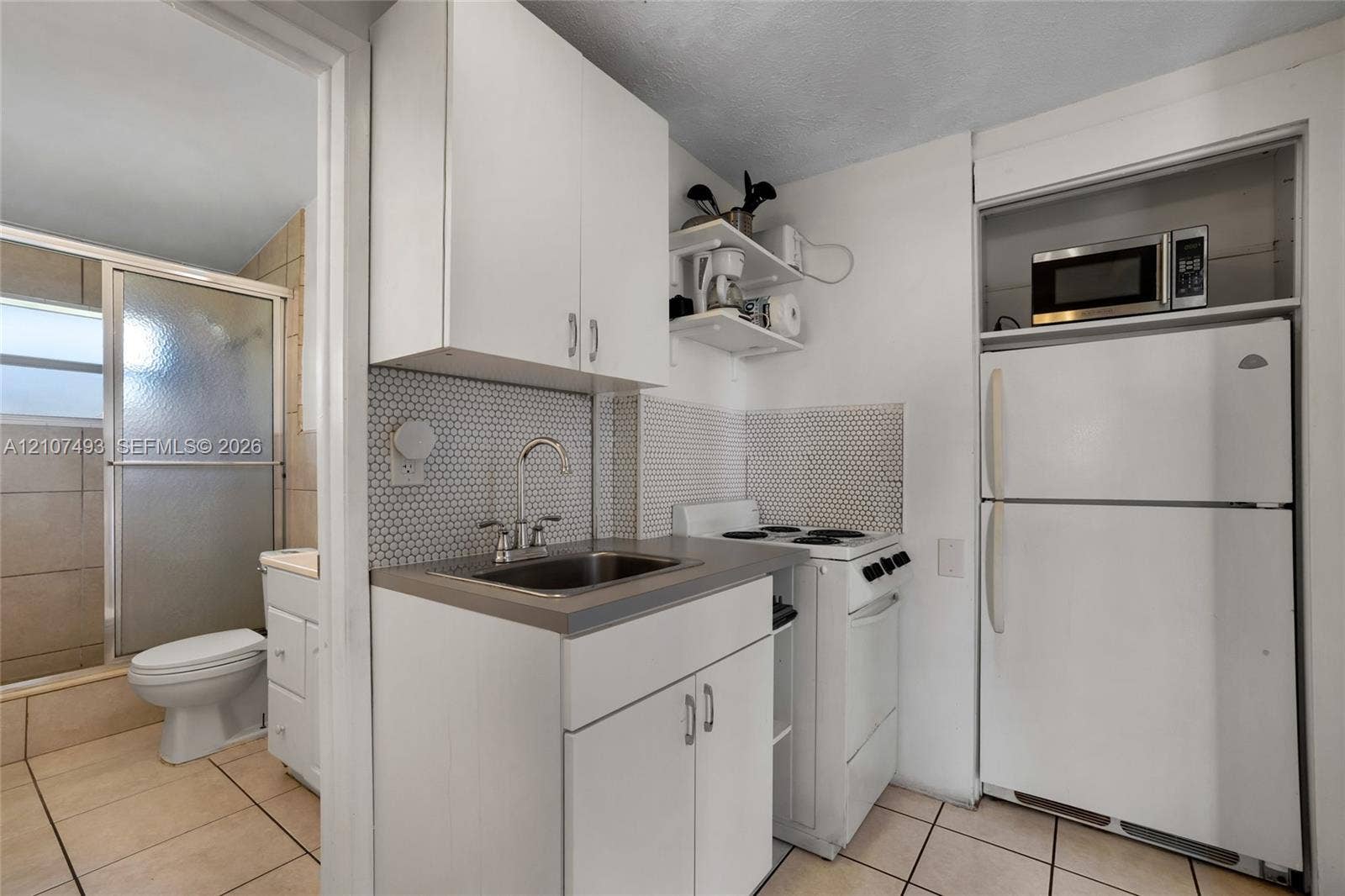 2645 NE 32nd Street, Fort Lauderdale, FL 33306 Compact kitchen featuring white cabinetry, hexagonal tile backsplash, stainless steel sink with arch faucet, and light-tone floor tiling